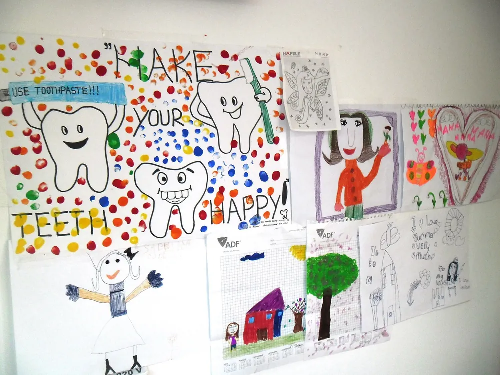 Perete cu desene făcute de copii: dinți zâmbitori și mesajul Make your teeth happy